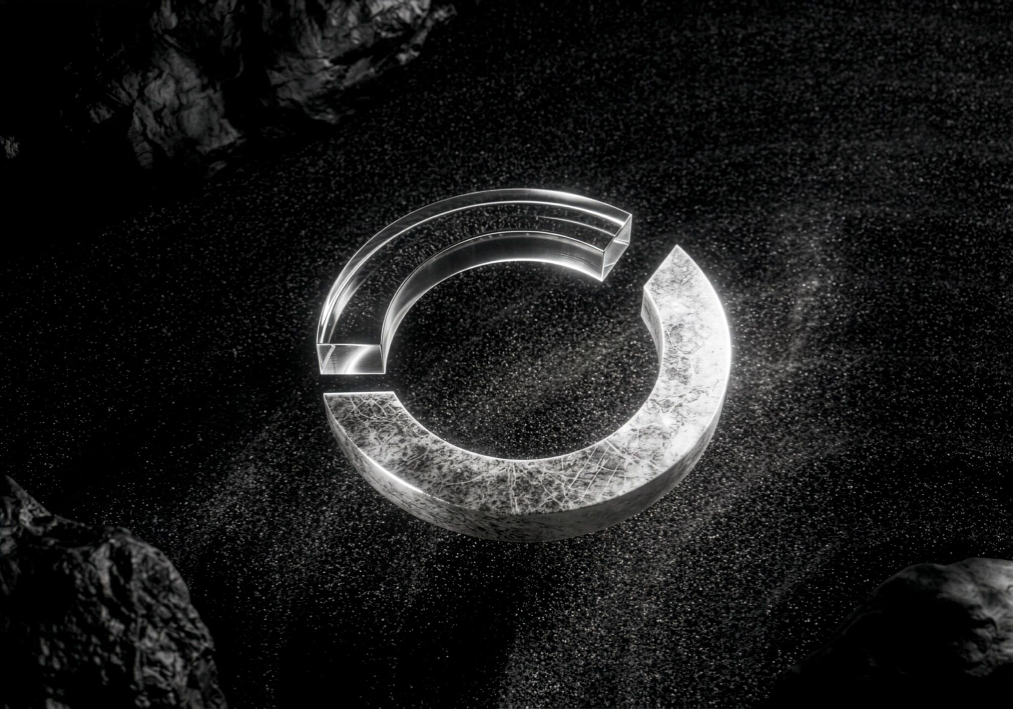 A 3D render of the open ring from the Envoy logo, one arc in clear glass and one in white stone, lying on dark sand between rocks.